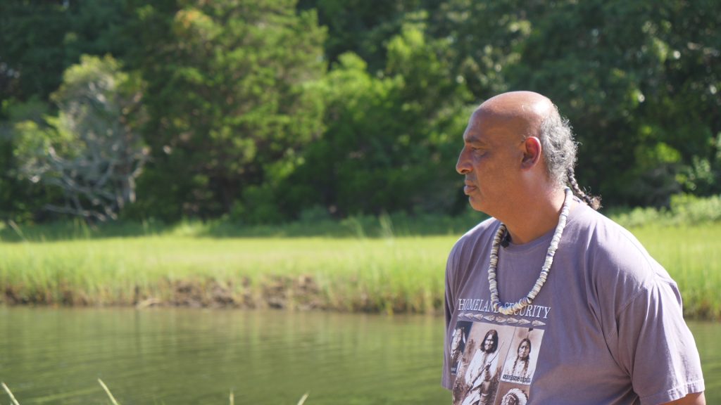 Buddy Pocknettin a purple t-shirt and wearing a wampum necklace by a Mashpee marsh